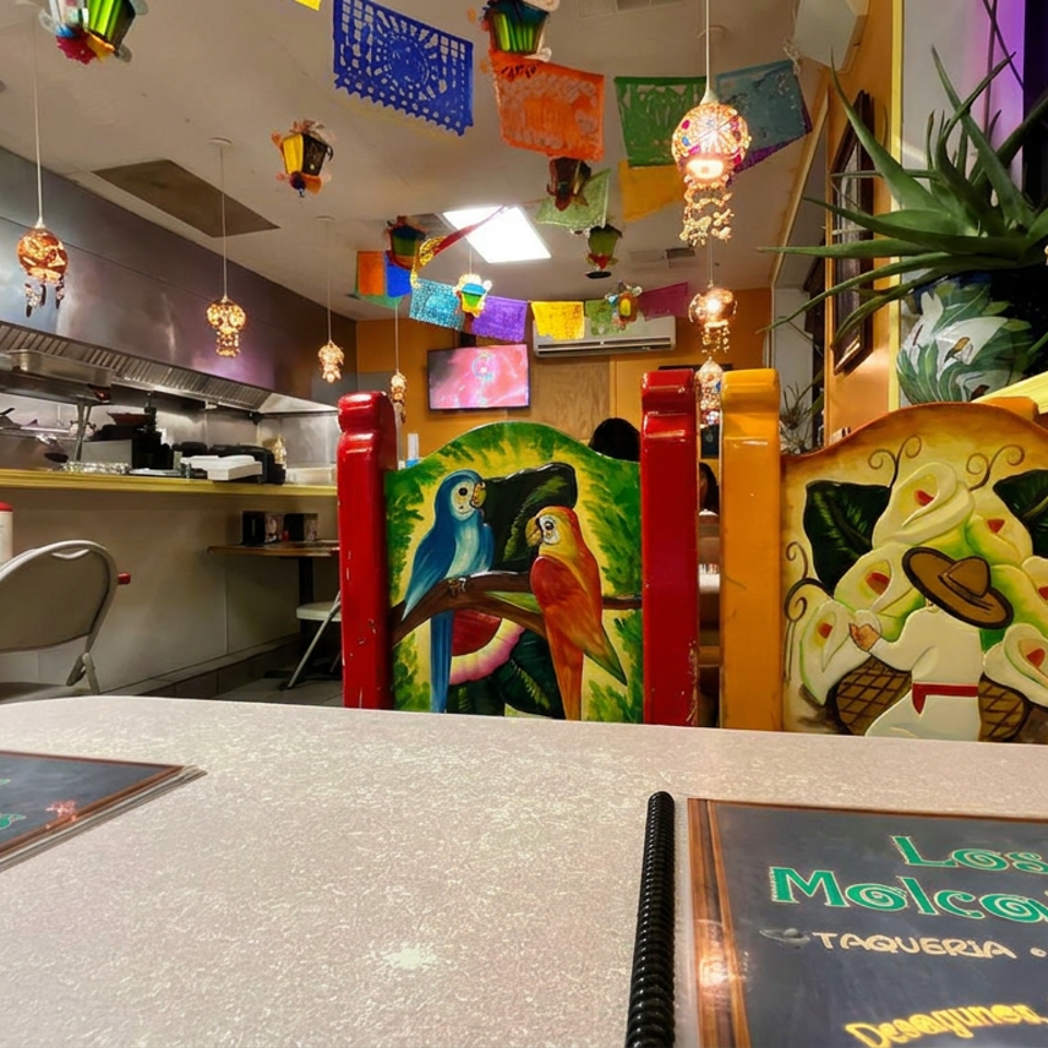 Colorful Mexican restaurant interior with hanging papel picado, painted parrot booths, open kitchen, and Los Molcajetes menus.