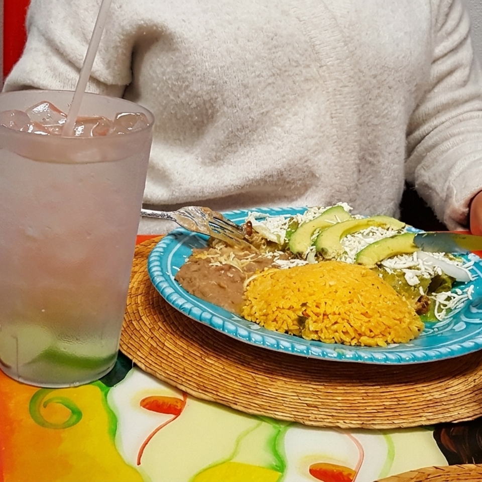 Mexican meal with rice, beans, avocado, and tortillas served on a colorful plate beside a lime drink and salsa.